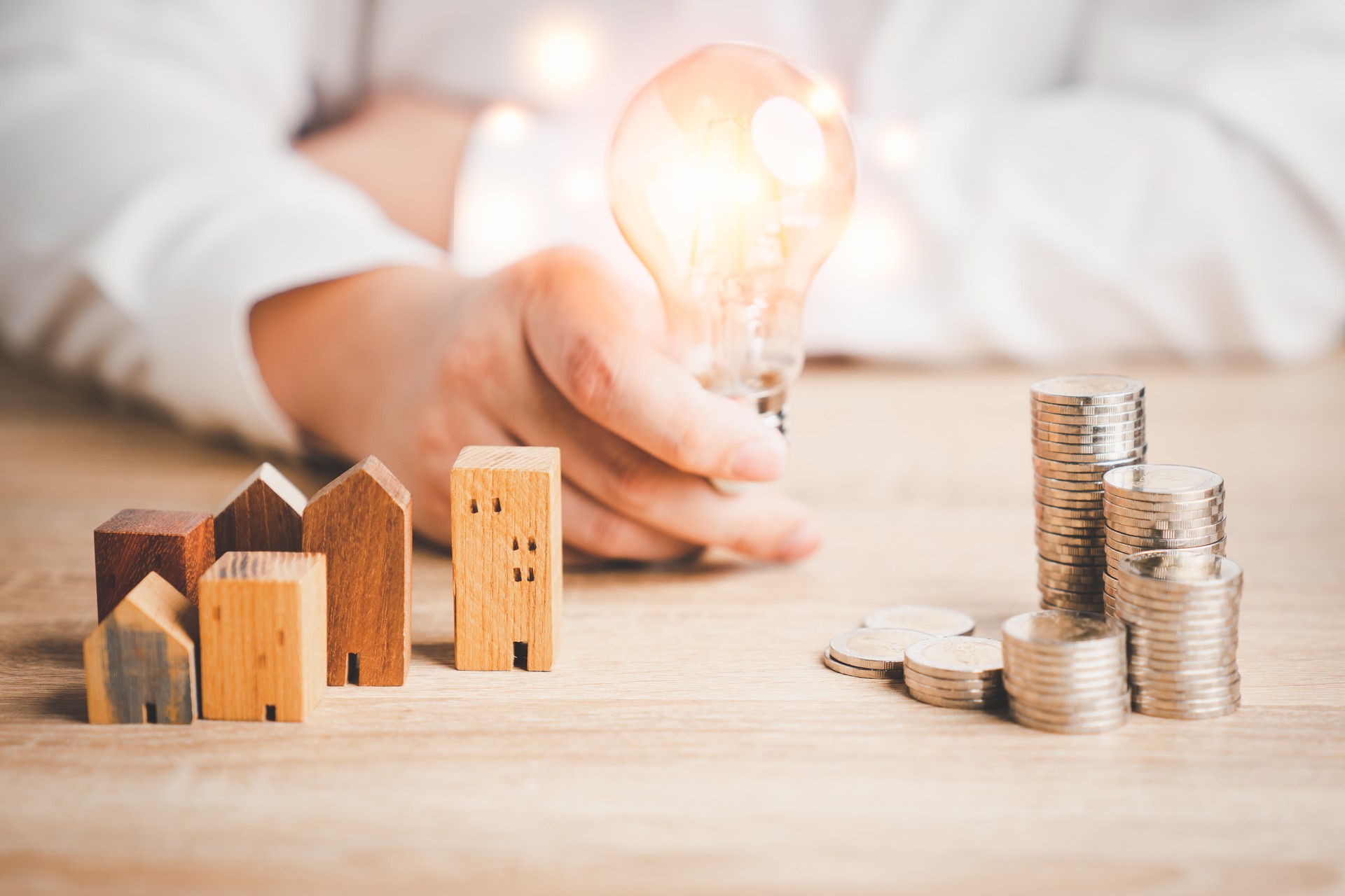 Modelo de casa de madera y fila de monedas con un hombre sosteniendo una bombilla. Gestión del dinero, plan financiero, idea de negocio e ideas creativas para ahorrar dinero.